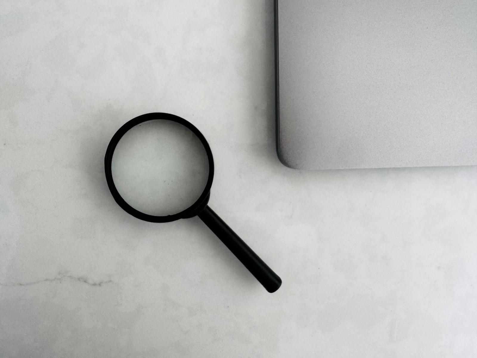A magnifying glass sits near a laptop on a table